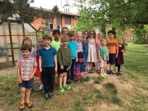 A group of children stands in the garden of the Philomath Montessori School. The school is visible behind them.